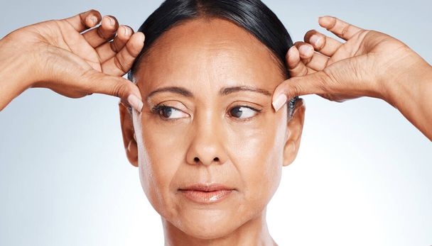 Skincare, beauty and senior woman thinking of wrinkles isolated on a grey studio background. Worry, cosmetic and face of a mature model feeling skin for anti aging, concern and idea on a backdrop. - Foto, Imagen