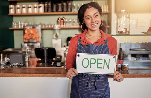 カフェやコーヒーショップでの販売を歓迎するためのオープンサインを持つ中小企業、肖像画や黒の女性。マーケティング、女性マネージャーや幸せな起業家は、小売店舗を宣伝またはオープンしながら笑顔. - 写真・画像