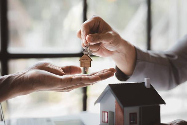 A home rental company employee is handing the house keys to a customer who has agreed to sign a rental contract, explaining the details and terms of the rental. Home and real estate rental ideas. - Foto, Imagem