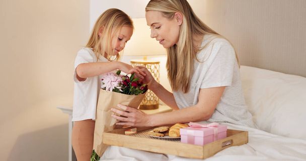 Πρωινό, παιδί και μαμά με ένα δώρο για τις μητέρες ημέρα το πρωί για να γιορτάσουν τη μαμά της στο σπίτι. Χαμογελάστε, Αγάπη και ευτυχισμένο κορίτσι δίνοντας στους γονείς ένα κουτί δώρου και ένα κρουασάν με μπισκότα σε ένα υπνοδωμάτιο. - Φωτογραφία, εικόνα