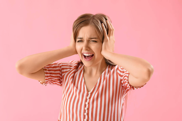 Angry young woman suffering from loud noise on pink background - Foto, immagini