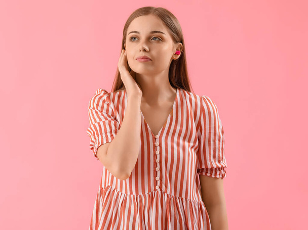Young woman with ear plugs on pink background - Foto, immagini