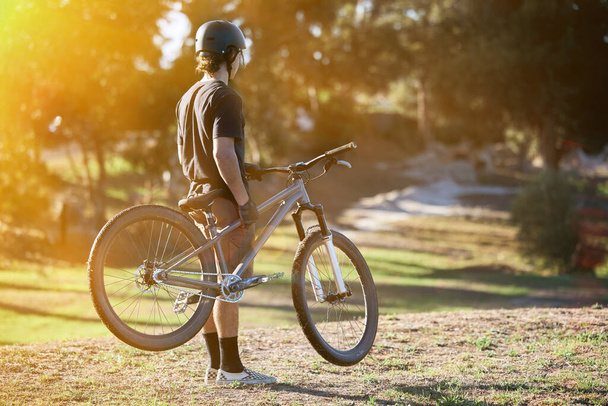 Bike, fitness and summer with a sports man outdoor in nature for leisure or recreation in summer. Back, bicycle and exercise with a male athlete standing on an open green field carrying his transport. - Fotoğraf, Görsel