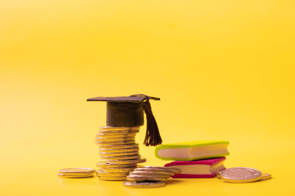 Mütze mit Münzen und Büchern auf gelbem Hintergrund. Einsparungen bei Bildungskonzept. - Foto, Bild