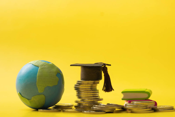 Graduated cap with coins and globe on yellow background. Savings for education concept. - Photo, image