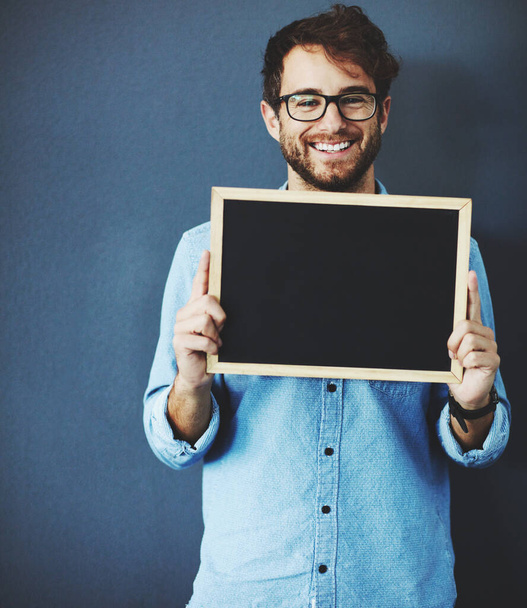Display your message on this prime spot. Studio portrait of a young man holding a blackboard against a grey background - Photo, Image