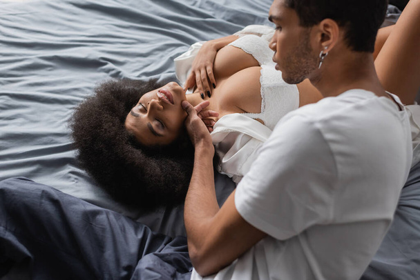 アフリカ系アメリカ人男性タッチ魅力的なガールフレンドとともにセクシー体嘘付きベッドの上に閉じられた目 - 写真・画像