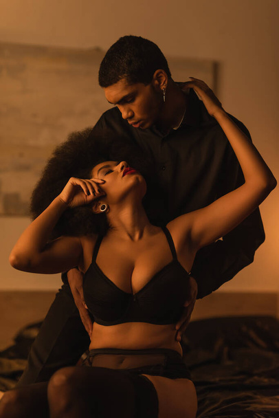 passionate african american woman in black bra embracing young boyfriend in black shirt - 写真・画像