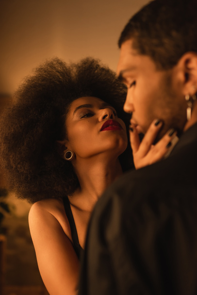 passionate african american woman touching face of young man while seducing him at home - 写真・画像