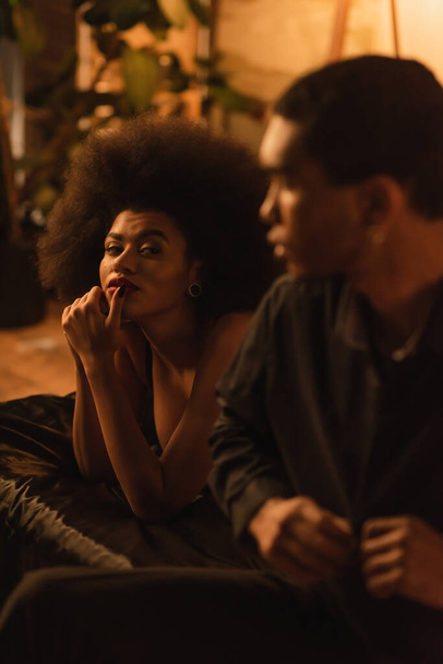 アフリカ系アメリカ人の女性見ます見ますぼやけたボーイフレンドunbuttoning黒シャツでベッドルーム - 写真・画像