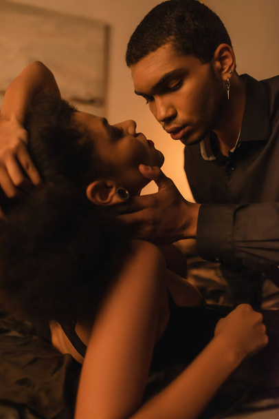 jeune homme afro-américain toucher le cou de la petite amie passionnée sur le lit - Photo, image
