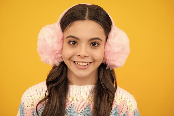 Schöne Teenie-Mädchen in einem warmen Ohrenschützer Ohrenklappen Hut und einem warmen Pullover. Ein Kind auf gelbem Hintergrund - Foto, Bild