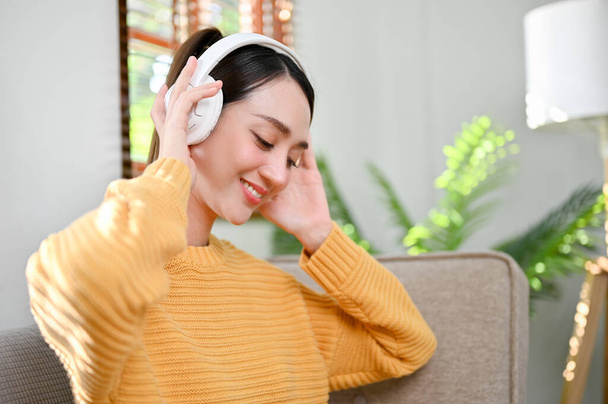 close-up image, Beautiful and charming millennial Asian woman wearing headphones, enjoying with the music, relaxing in her living room. - Фото, зображення