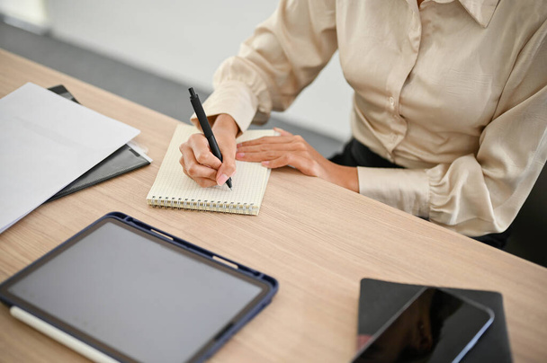 Верхній вигляд професійної азіатської комерсантки робить нотатки або складає список на своєму блокноті при своєму офісному столі.. - Фото, зображення