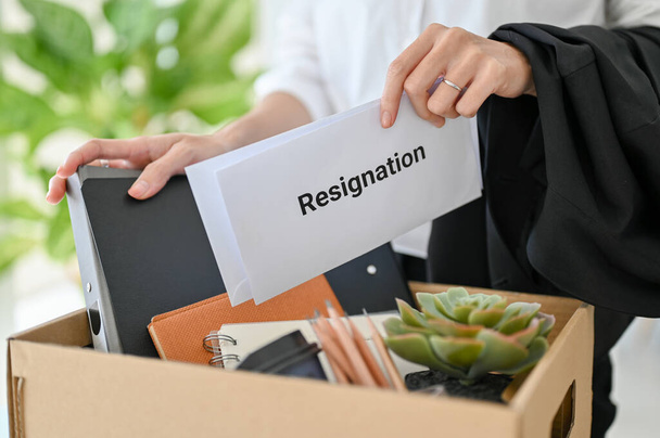 A businesswoman with a resignation letter in her hand and her stuff in a cardboard box. moving, quit a job, unemployment, career failure. close-up image - Foto, Imagem