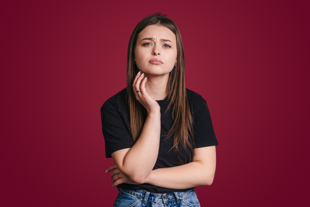 Portrait of displeased young woman with brunette hair looking frustrated at camera doesnt agree with somebodys opinion isolated over crimson studio background - Photo, image