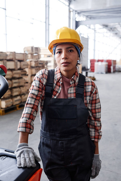 Young serious female engineer in workwear standing by cart with package in front of camera in distribution warehouse - Foto, imagen