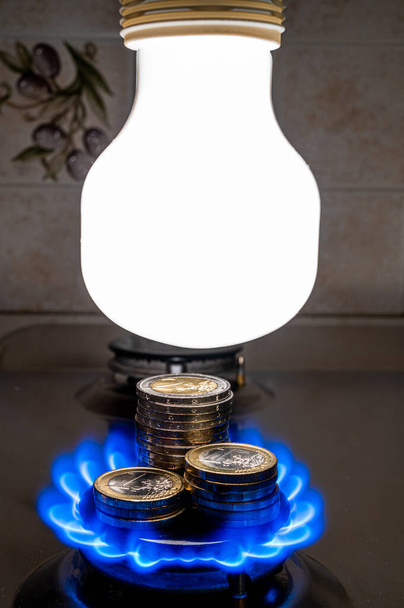 Light bulb on and lit gas cooker, with coins next to it. Energy and gas costs, cost increases. - Fotó, kép