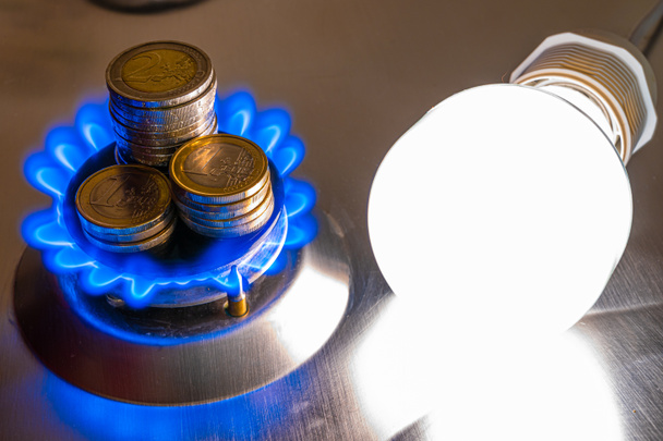 Light bulb on and lit gas cooker, with coins next to it. Energy and gas costs, cost increases. - Foto, Imagen
