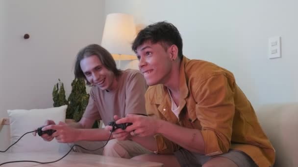 Two young male friends using controllers while playing video games together at home - Materiał filmowy, wideo