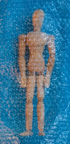 Wooden toy mannequin of man under the air bubble wrap. Blue background. - Foto, imagen