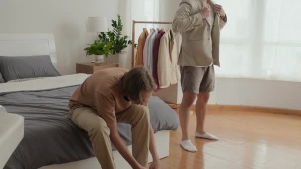 Tilt up shot of two male friends in their early 20s getting dressed in bedroom before going out - Materiał filmowy, wideo
