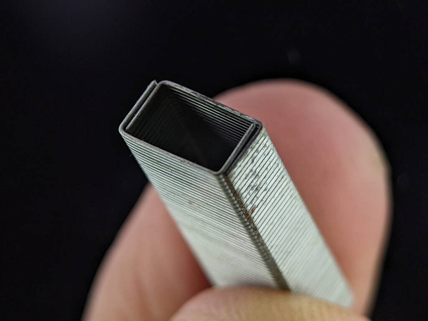 Closeup finger holding staplers bullet on a black background - Foto, Imagen