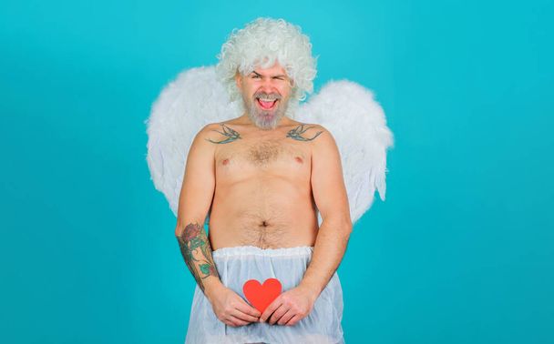 Naughty cupid. Valentines day celebration. Male Angel in angelic wings with red paper heart - Zdjęcie, obraz