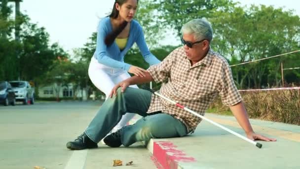 Asian blind old man walking with a cane blind accident accident stumbles on the sidewalk falls down receives first aid help from a kind beautiful woman to get up with concern. - Filmati, video