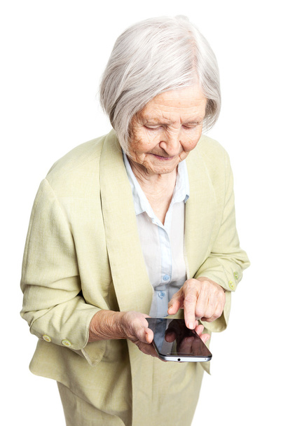 Seniorin benutzt Handy, während sie vor weißem Hintergrund steht - Foto, Bild