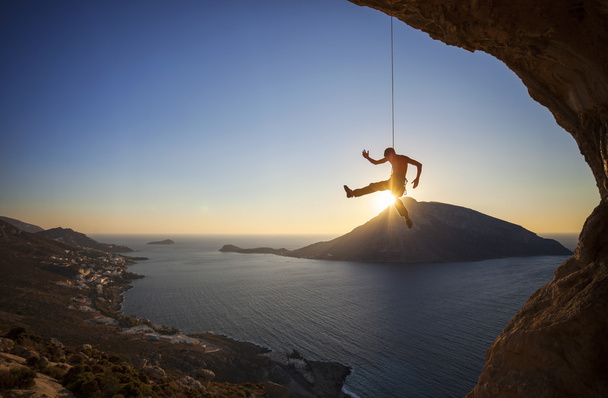 Scalatore di roccia appeso alla corda mentre si arrampica al tramonto, con l'isola Telendos sullo sfondo
 - Foto, immagini