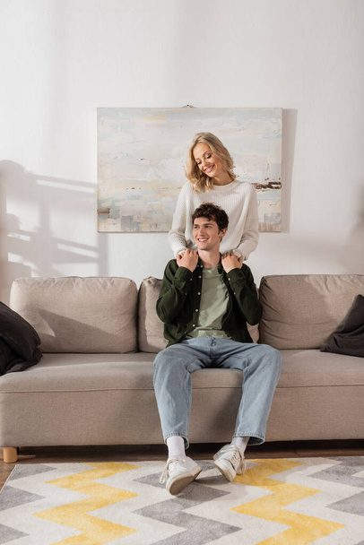 young cheerful woman in sweater hugging boyfriend in living room  - Foto, immagini