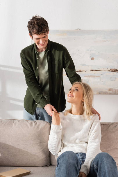 curly young man and blonde woman holding hands in living room  - Фото, зображення