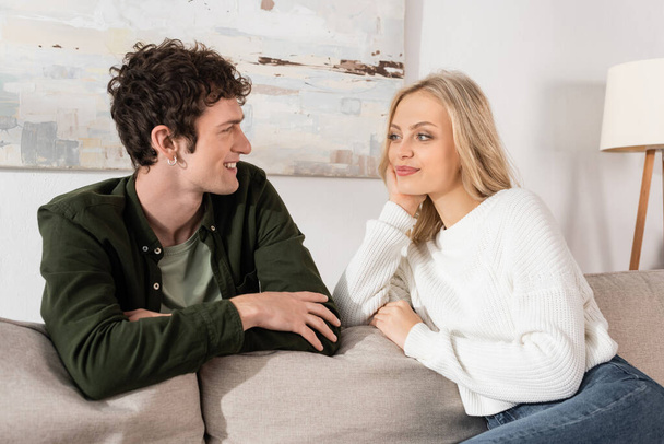 young woman with blonde hair looking at curly boyfriend in living room  - Photo, Image