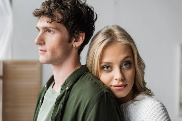 portrait of blonde woman in white sweater leaning on back of curly young man - Foto, imagen
