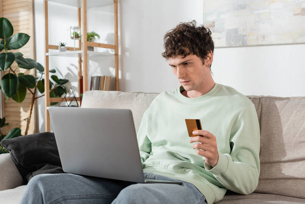 curly young man holding credit card while doing online shopping on laptop  - Photo, image