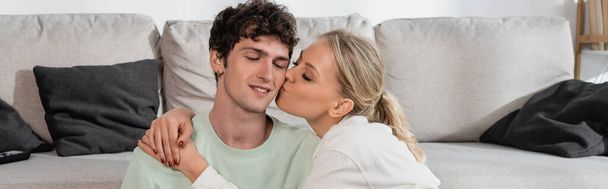 onnellinen blondi nainen suudella poski poikaystävä olohuoneessa, banneri - Valokuva, kuva