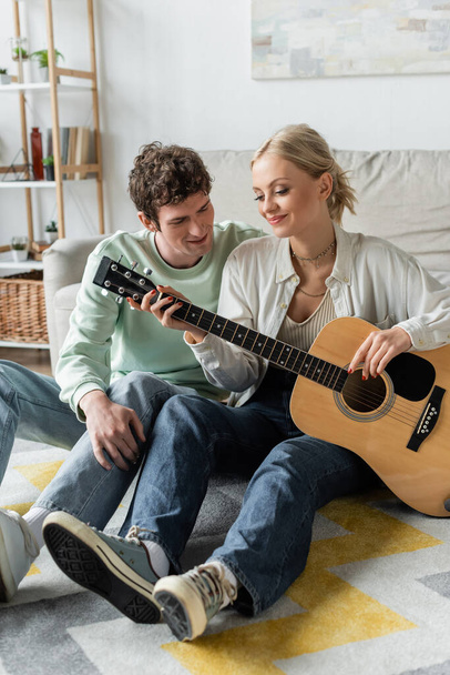 cheerful blonde woman playing acoustic guitar near curly boyfriend  - Photo, Image