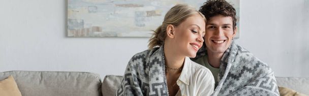 happy young man and woman covered in blanket smiling in living room, banner  - Foto, Imagem