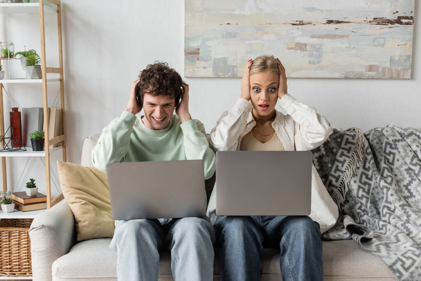 stressed young man and woman looking at laptops while sitting on couch  - Φωτογραφία, εικόνα
