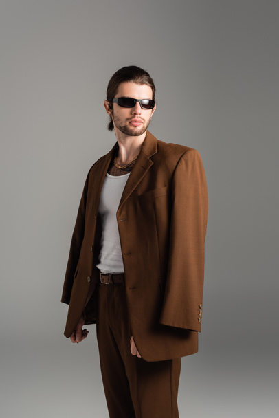 Fashionable man in sunglasses posing in brown suit isolated on grey  - Fotografie, Obrázek