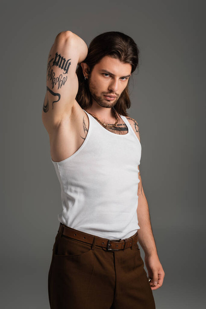 Muscular and tattooed model in white tank top looking at camera isolated on grey  - Φωτογραφία, εικόνα