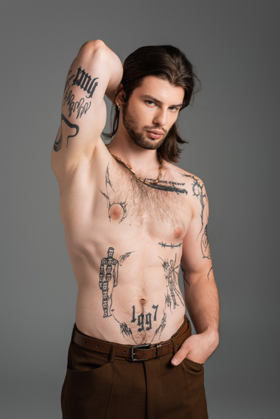 Muscular and tattooed man in pants posing isolated on grey  - Fotó, kép