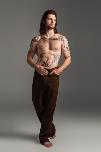 Full length of tattooed and shirtless man with tattoo on body on grey background - 写真・画像