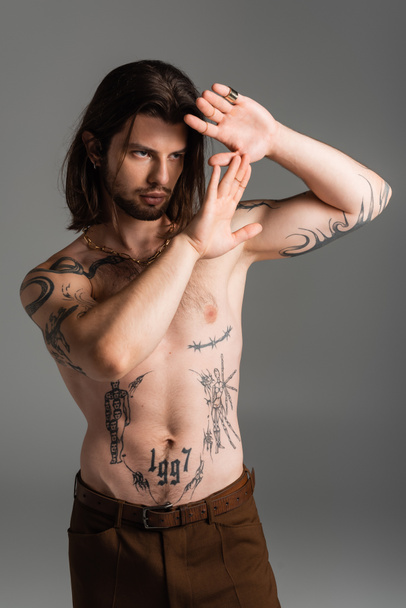 Bearded long haired model with tattoo on torso posing isolated on grey  - Foto, imagen