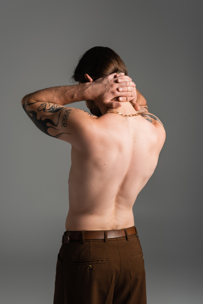 Shirtless and tattooed model touching neck isolated on grey  - Photo, Image