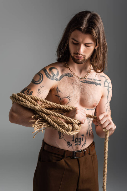 Shirtless and tattooed model holding rope isolated on grey  - Φωτογραφία, εικόνα