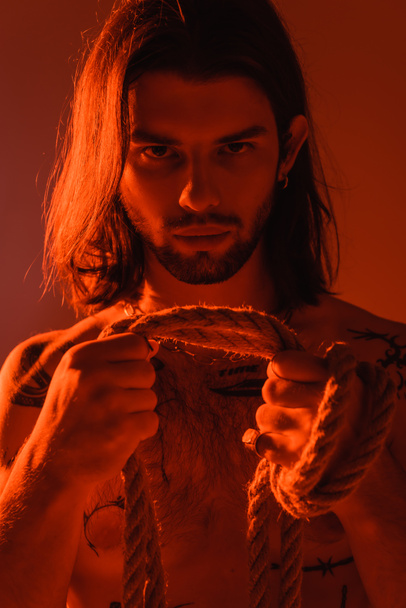 Portrait of tattooed man holding rope isolated on red  - Φωτογραφία, εικόνα