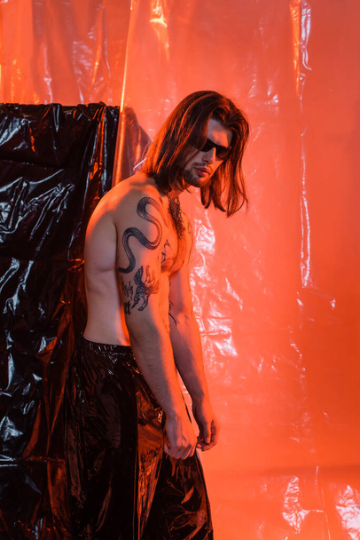 Tattooed man in sunglasses standing near cellophane  - Photo, Image