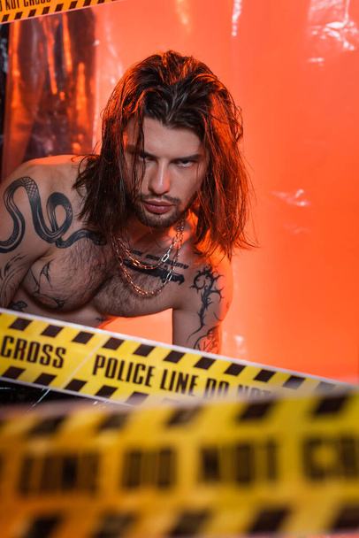 Long haired tattooed man looking at camera near police line  - 写真・画像